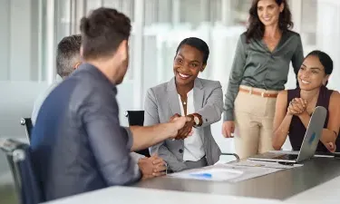 Human resources professional shaking hands with a candidate during a job interview in a modern office setting.